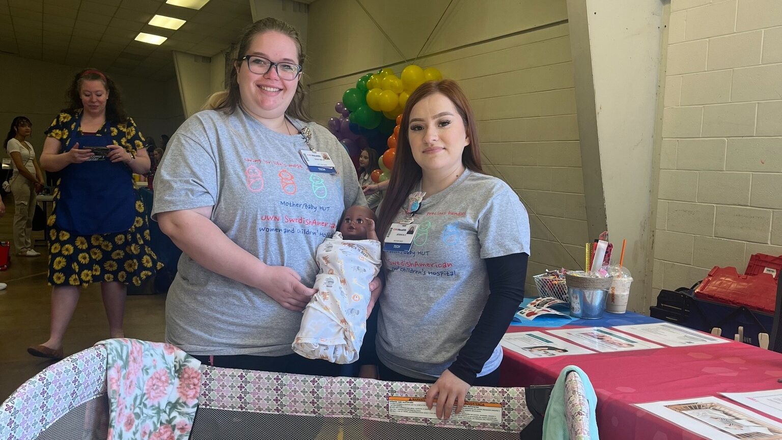 Two employees with baby doll, demonstrating safe sleep practices.